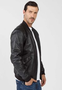 Zwart leren bomberjack met een ritssluiting, geribde manchetten en twee zijzakken. Draag het over een wit T-shirt. Soepele textuur, casual pasvorm.