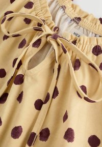 Gelber Stoff mit unregelmäßigen dunkelvioletten Punkten, ausgestattet mit einem Kordelzug und elastischem Bund.