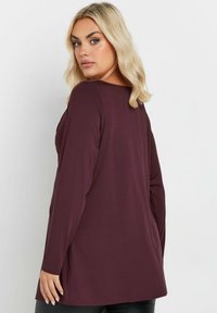 Långärmad topp i mörk vinröd tyg. Har en rundad halsringning och en avslappnad passform, med svängda sprund i fållen för ökad rörelsefrihet.