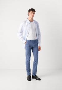 Chemise à rayures bleu clair, débardeur blanc, pantalons bleu clair, chaussures noires, pose debout, tissu lisse, coupe ajustée.