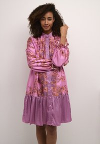 Dlhé ružové šaty s kvetinovými vzormi, volánovými rukávmi, nariasenými detailmi, zapínaním na gombíky a vrstveným volánovým lemom. Textúrová látka.