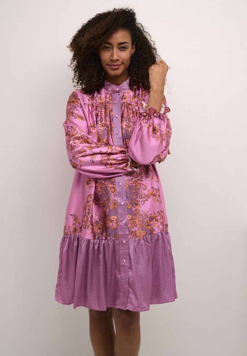 Dlhé ružové šaty s kvetinovými vzormi, volánovými rukávmi, nariasenými detailmi, zapínaním na gombíky a vrstveným volánovým lemom. Textúrová látka.