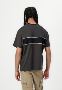Dark gray T-shirt with a round neck, short sleeves, and a contrasting horizontal navy stripe across the back. Cotton material with smooth texture.
