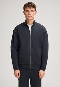 Felpa con zip blu navy e colletto alto, maniche lunghe e polsini a coste. Realizzata in tessuto morbido con un design minimale, dotata di tasche laterali.