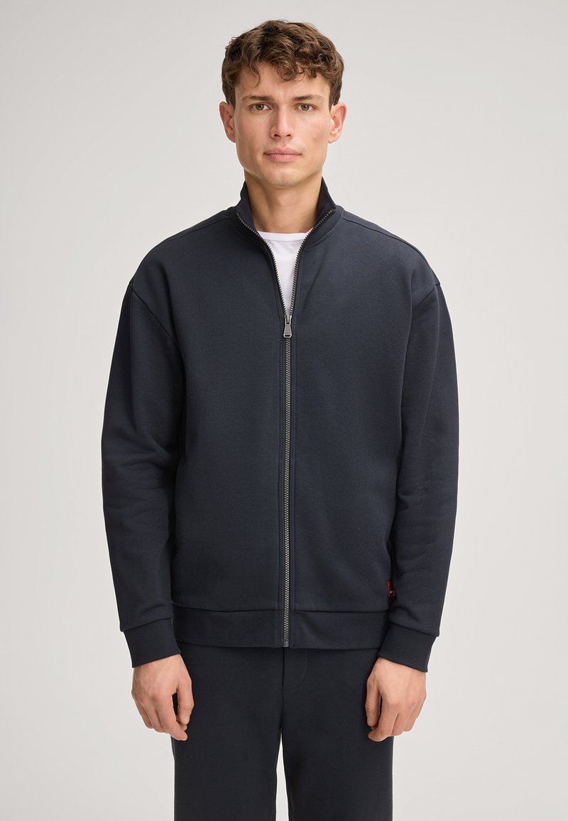 Felpa con zip blu navy e colletto alto, maniche lunghe e polsini a coste. Realizzata in tessuto morbido con un design minimale, dotata di tasche laterali.