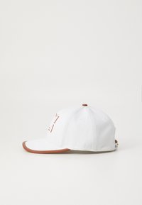 White baseball cap with a brown brim and stitching, featuring an embroidered logo on the front and ventilation holes on top.