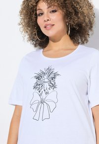 Camiseta blanca de algodón con un dibujo en línea negra de la cabeza de un pájaro y un gran lazo debajo. Manga corta y escote redondeado.