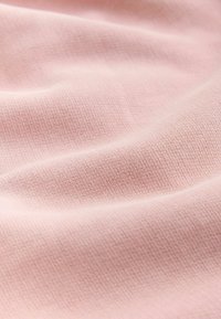 Tissu tricoté rose doux avec une texture fine et uniforme et de légères plis créant des ombres douces à la surface.