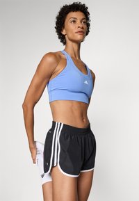 Den sporty antrekk inkluderer en lyseblå sports-BH og svarte shorts med hvite detaljer, laget av fleksible materialer for komfort og bevegelse.