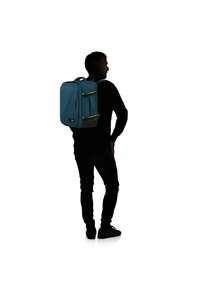 Blå ryggsäck med två gula accenter, rektangulär form, framficka med dragkedja, justerbara remmar och ett handtag på toppen för bärande.