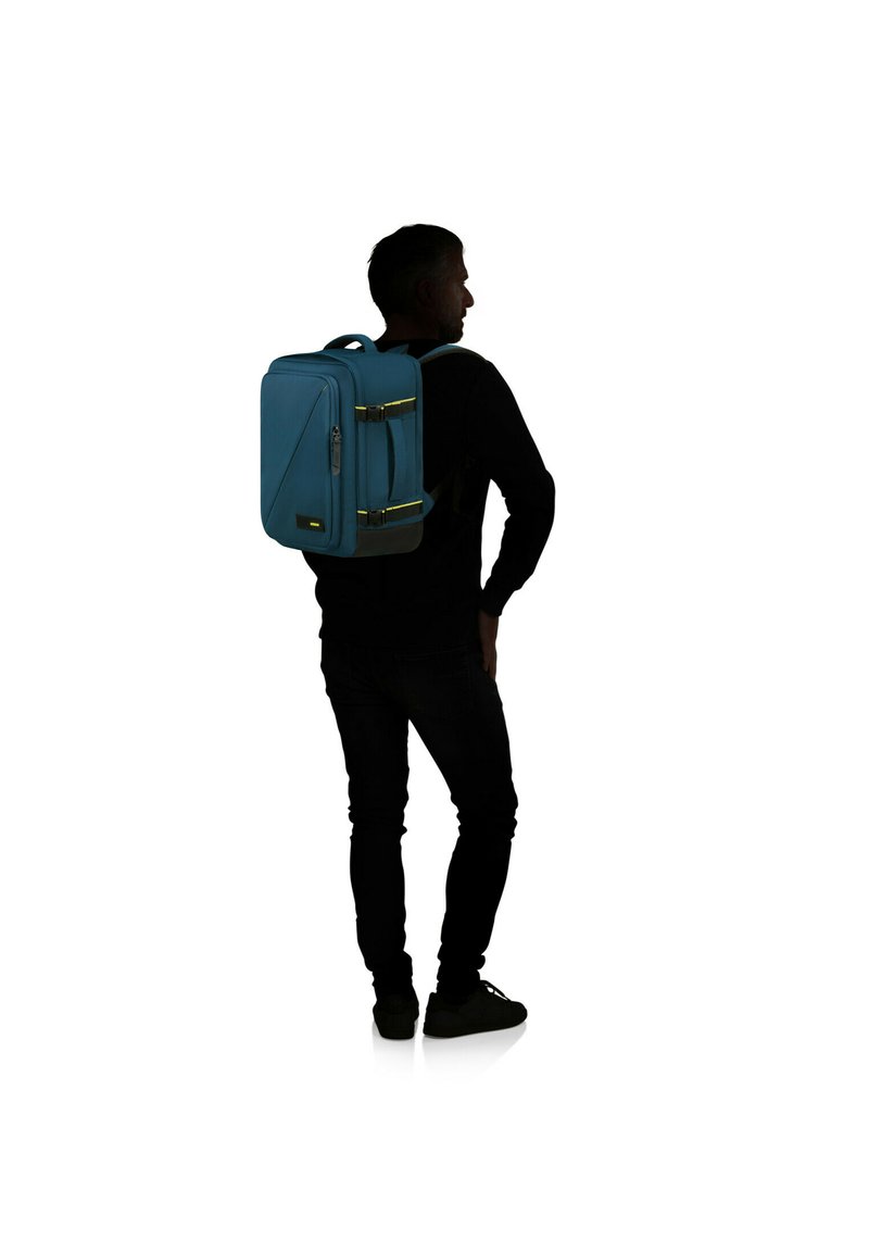 Blå ryggsäck med två gula accenter, rektangulär form, framficka med dragkedja, justerbara remmar och ett handtag på toppen för bärande.