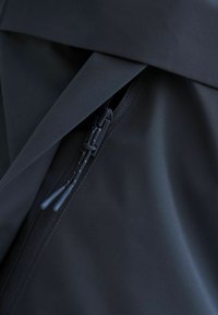 Zwarte stof met een gladde textuur, voorzien van een zichtbare ritssluiting en verstelbare trekkoordjes, met een overlappend ontwerp-element.