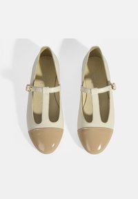 Cremefarbene Lederschuhe mit einer beigefarbenen lackierten Spitze. Sie verfügen über einen T-Riemen mit einer goldenen Schnalle und ausgeschnittenen Seiten für Belüftung.