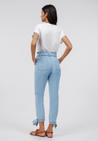 Pantaloni in denim azzurro chiaro a vita alta con fascia elastica e dettagli con fiocco ai polsini, dotati di due tasche posteriori e una superficie liscia.