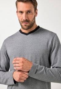 Szara koszula z długim rękawem i czarnym kołnierzykiem w kształcie litery V. Wzór w paski na całej powierzchni, z subtelnym logo na mankiecie rękawa. Miękki, teksturowany materiał.