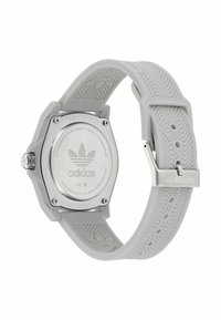 Pilkas silikono dirželis laikrodis su aštuonkampiu nerūdijančio plieno korpusu ir sidabro spalvos nugarėlė. Ant laikrodžio yra Adidas logotipas ir tekstūruotas dirželio raštas.
