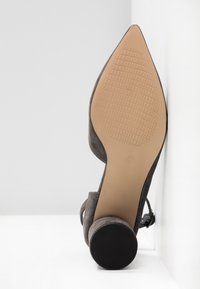 Chaussure femme en daim gris à bout pointu avec bride cheville, talon bloc et semelle beige texturée tournée vers le haut.