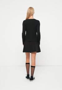 Top negro de manga larga combinado con una falda negra acampanada. La modelo lleva calcetas translúcidas hasta la rodilla y zapatillas negras. Diseño simple y minimalista.