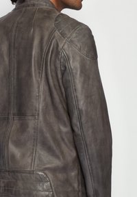 Graue Lederjacke mit glatter Textur, tailliertem Design, dezenten Schulterakzenten und sichtbaren Steppnähten entlang der Nähte und Taschen.