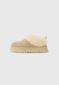 Zapato beige tipo slip-on con suela gruesa y forro de piel sintética crema alrededor del tobillo, diseñado para brindar calidez y comodidad.