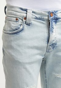 Light blue faded denim jeans with front pockets, copper rivets, belt loops, and slight distressing on the thigh area.