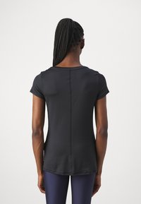 T-shirt de sport noir à manches courtes, en tissu texturé, avec un col rond et une couture centrale. Convient pour les vêtements de sport, associé à des leggings bleu marine.