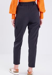 Person wearing black cargo pants with side pockets, orange sweater, and beige white sneakers standing against a plain light background.