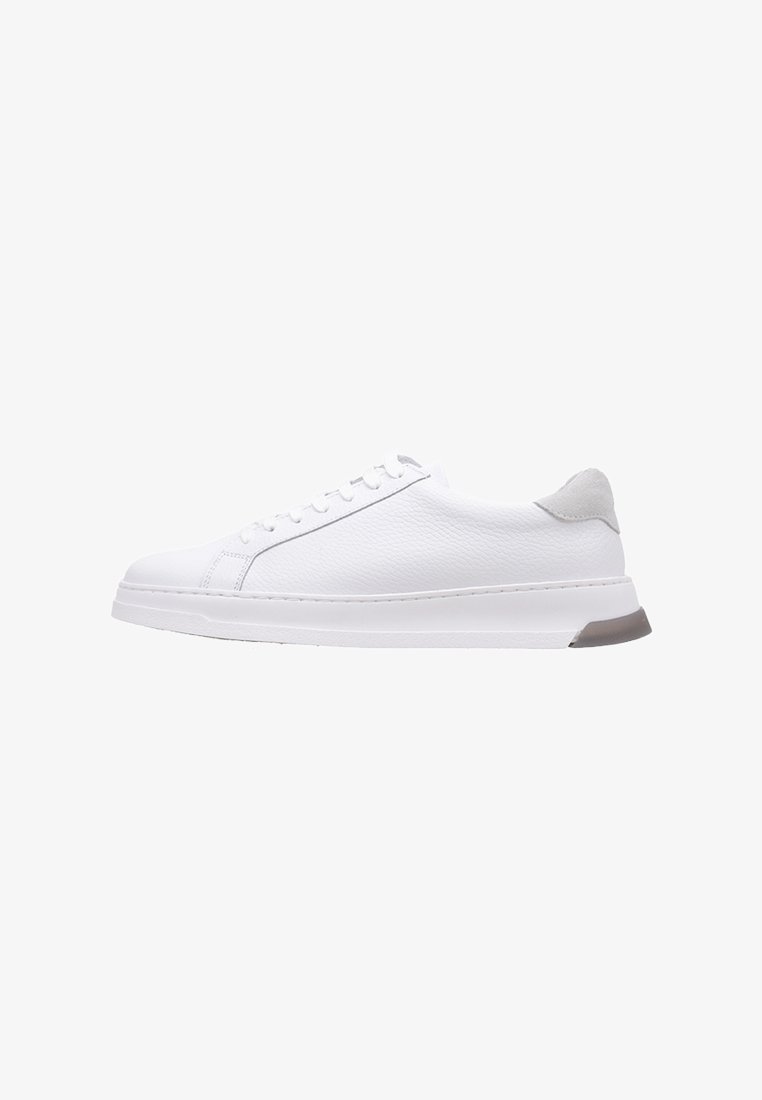 Zapatilla de cuero blanca con textura suave, que presenta una puntera redondeada, seis ojetes, un acento en el talón gris y una suela blanca resistente.