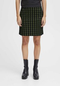 Zwart en groen gestreepte rok met een rechte snit, gekleed tot de knie, gemaakt van een gestructureerde stof. Gestyled met zwarte enkellaarzen.