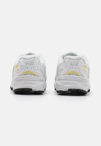 Baltos sportinės bateliai su tinklinėmis viršutinėmis dalimis, paminkštintu apvadu ir guminėmis padais. Geltoni akcentai papildo dizainą. Galinis vaizdas.