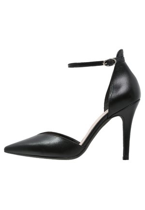 Zapato de tacón alto de cuero negro con punta afilada, tirante en el tobillo y diseño con cortes laterales. Textura suave, tacón de aproximadamente 10 cm.