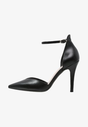 Bottines noires en cuir verni à talons hauts avec bout pointu, brides autour de la cheville et découpe sur le côté. Texture lisse, talon d'environ 10 cm.