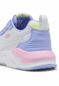 Zapatilla blanca de malla con detalles en tonos pastel morado, rosa y verde, logo blanco de Puma y suela gruesa blanca vista desde la parte trasera.