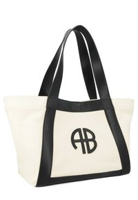 Sac en toile crème avec des accents en cuir noir. Présente un logo brodé bien en vue et des doubles sangles pour l'épaule.