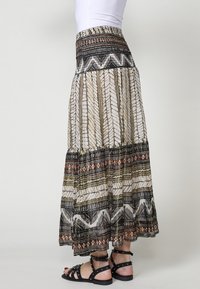 Maxi rok met een gelaagd ontwerp in wit, zwart en aardetinten. Bevat geometrische patronen en een elastische tailleband. Gepaard met zwarte sandalen.
