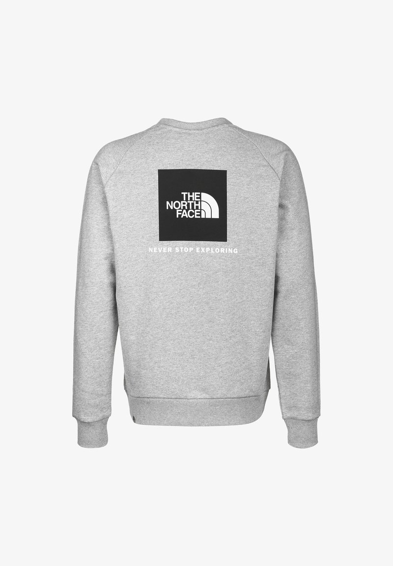 Sweatshirt gris avec col rond et manches longues. Présente un logo carré noir avec le texte "THE NORTH FACE" et "NEVER STOP EXPLORING".