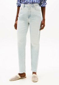 Jeans azzurri chiari a vita alta con gamba dritta, caratterizzati da un orlo grezzo e un leggero sbiadimento, abbinati a scarpe slip-on intrecciate beige.
