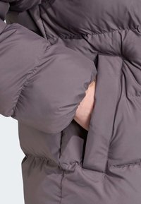 Halli puffer-jakk seljaosa, mille juures on nähtav käsi, mis ulatub küljetaskusse. Omab quiltitud struktuuri ja elastseid manžette soojustamiseks.