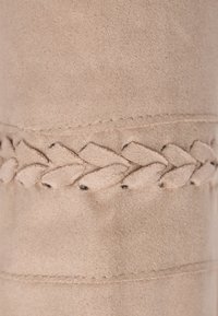 Beige suéd anyag fonott díszvarrással. Sima tapintású és diszkrét fényű, tiszta, egyszerű varrási részletekkel.