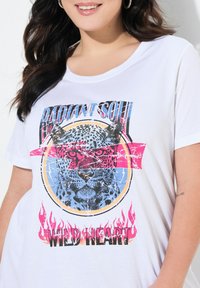 Camiseta de algodón blanca con un gráfico de un leopardo con acentos rojos y azules, incluyendo el texto "ALMA RADIANTE" y "CORAZÓN SALVAJE" en la parte inferior.