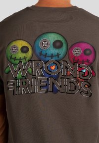 Camiseta gris con tres personajes de calaveras coloridos y en estilo de dibujos animados, con ojos de botón. El texto dice "AMIGOS ERRÓNEOS" en letras negritas debajo.