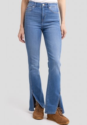 Jeans de mezclilla azul claro de corte acampanado con una cintura alta y detalle de dobladillo partido. Cuenta con cinco bolsillos, herrajes dorados y una textura suave.
