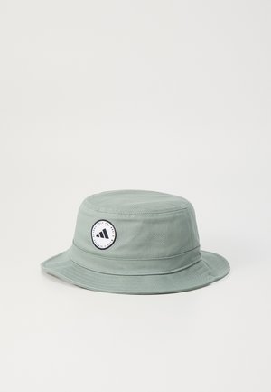 Chapeau seau vert clair en coton avec un patch rond arborant un design triangulaire et du texte. Large bord, forme structurée, tissu texturé.