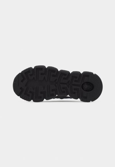 Μαύρη σόλα παπουτσιού με βαθύ γεωμετρικό ανάγλυφο μοτίβο και κυκλική υφή κοντά στη φτέρνα, σε απλό φωτεινό φόντο.