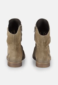 Par de botas de ante marrón claro hasta el tobillo con cremalleras laterales, forro interior visible y tacones de madera bajos, mostradas desde atrás sobre un fondo blanco.