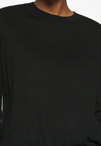 Svart stickad tröja med en klassisk rund halsdesign. Mjuk textur, rena linjer och långa ärmar skapar en enkel, mångsidig silhuett.