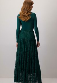 Abito lungo verde con top aderente in un materiale liscio e una gonna in pizzo a strati con un motivo testurizzato.