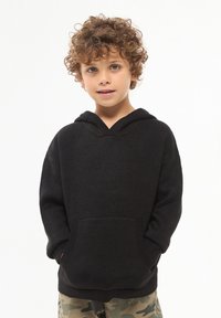 Czarna bluza z kapturem wykonana z teksturowanej tkaniny, z kieszenią z przodu i ściągaczami na rękawach. Dziecko stoi na jasnym tle.