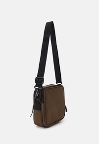 Borsa a tracolla marrone realizzata in tessuto resistente, con forma quadrata, cinturino regolabile nero, chiusura con zip e tasca laterale con zip.