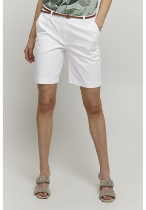 Valkoiset muotoiltut shortsit sivutaskuilla, joissa on ruskea vyö. Silkkinen puuvillakangas klassisella suoralinjaisella leikkauksella. Peep-toe-sandaalit hillityssä beigeessä.